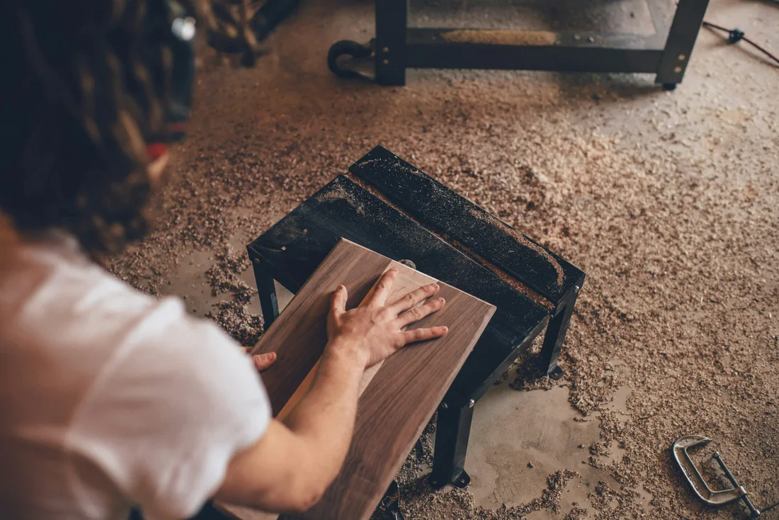 Woodworker shaping a board at a sawdust-covered workshop bench